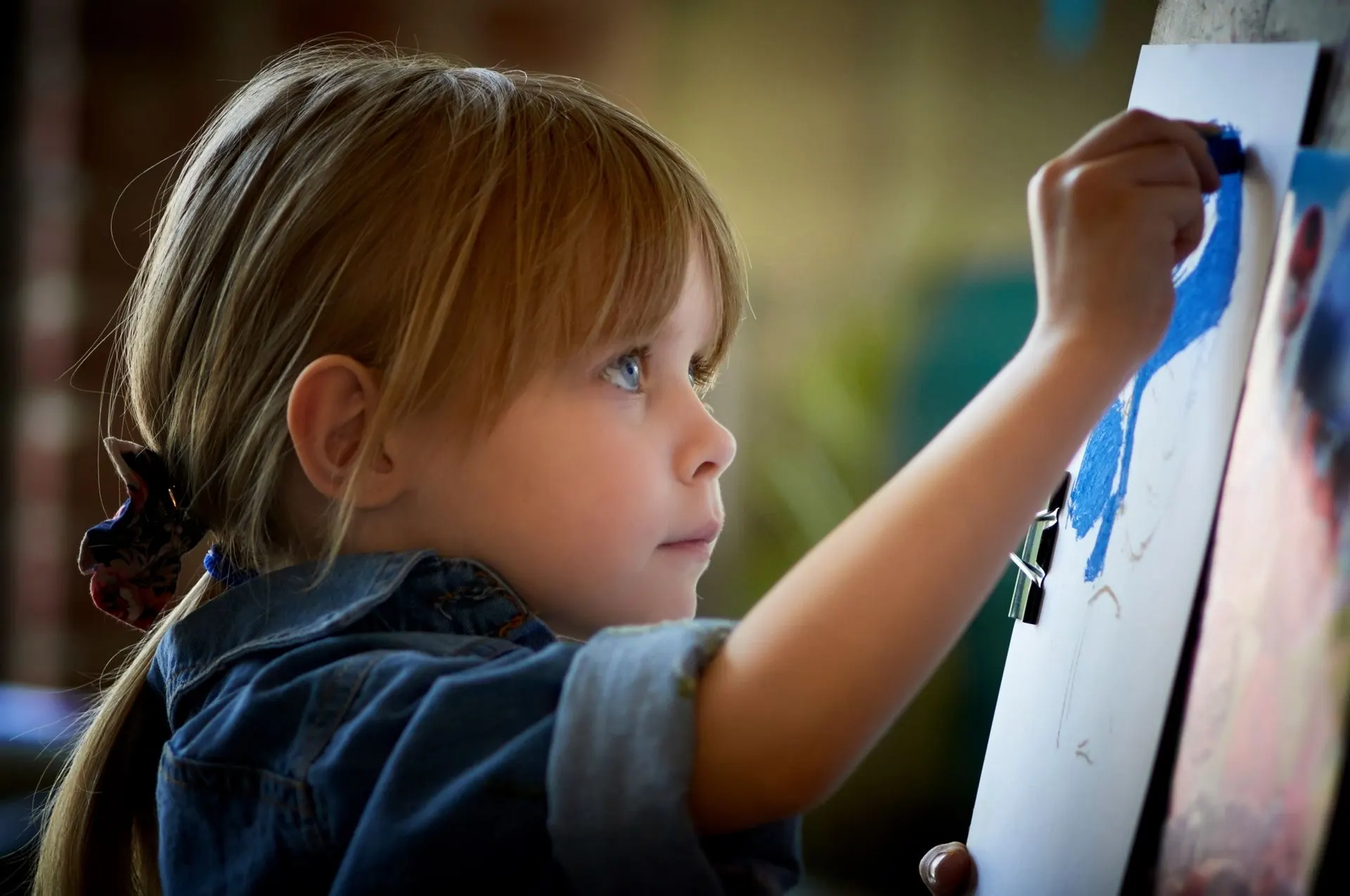 A young child absorbed in painting under warm, moody light